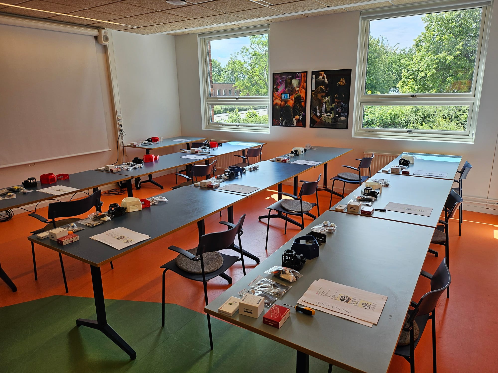 Photo of the classroom before the start of the workshop. Materials are scattered across three rows of desks.